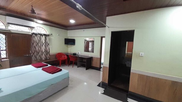 A room with a bed, a desk, and a TV. - Hotel Gokarna International (Kumta)