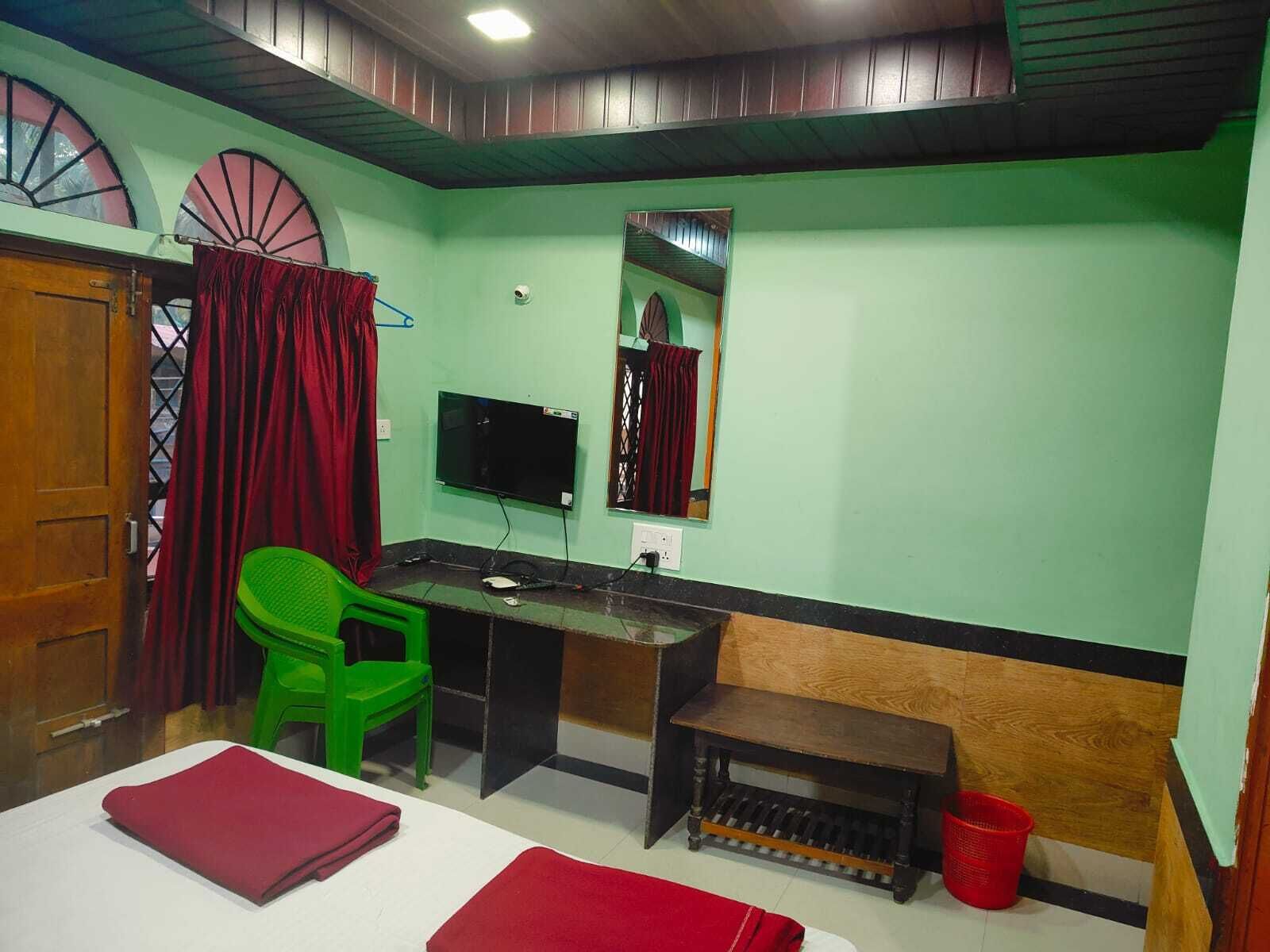 Quarto com uma cama, uma escrivaninha, uma cadeira, uma televisão e uma janela com cortinas.