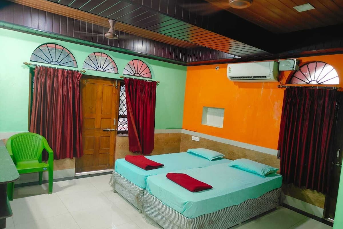 A room with two beds, a green chair, and an air conditioning unit.