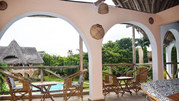 An outdoor patio with wicker furniture, a pool, and a thatched-roof building in the background.