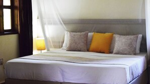 A neatly made bed with a grey headboard, white bedding, and two pillows in shades of grey and orange.
