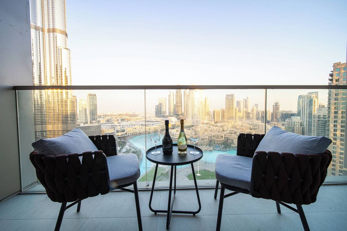 A balcony with two chairs and a table, overlooking a cityscape with tall buildings.
