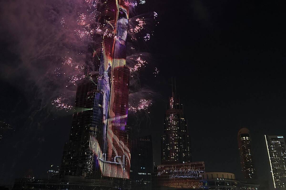 A nighttime cityscape with a prominent tower illuminated with colorful lights and fireworks.