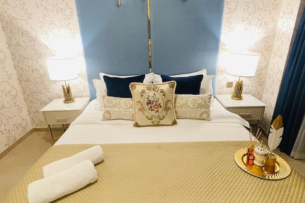A hotel room with a large bed, two bedside tables with lamps, a decorative pillow, and a tray with a bottle and a candle. - One Lux Stay Grande Signature Residences (Dubai)