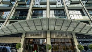 Korkea kerrostalo, jossa on moderni julkisivu, suuret lasi-ikkunat ja huomiota herättävä sisäänkäynti, jonka yläpuolella on teksti ”GRANDE”.