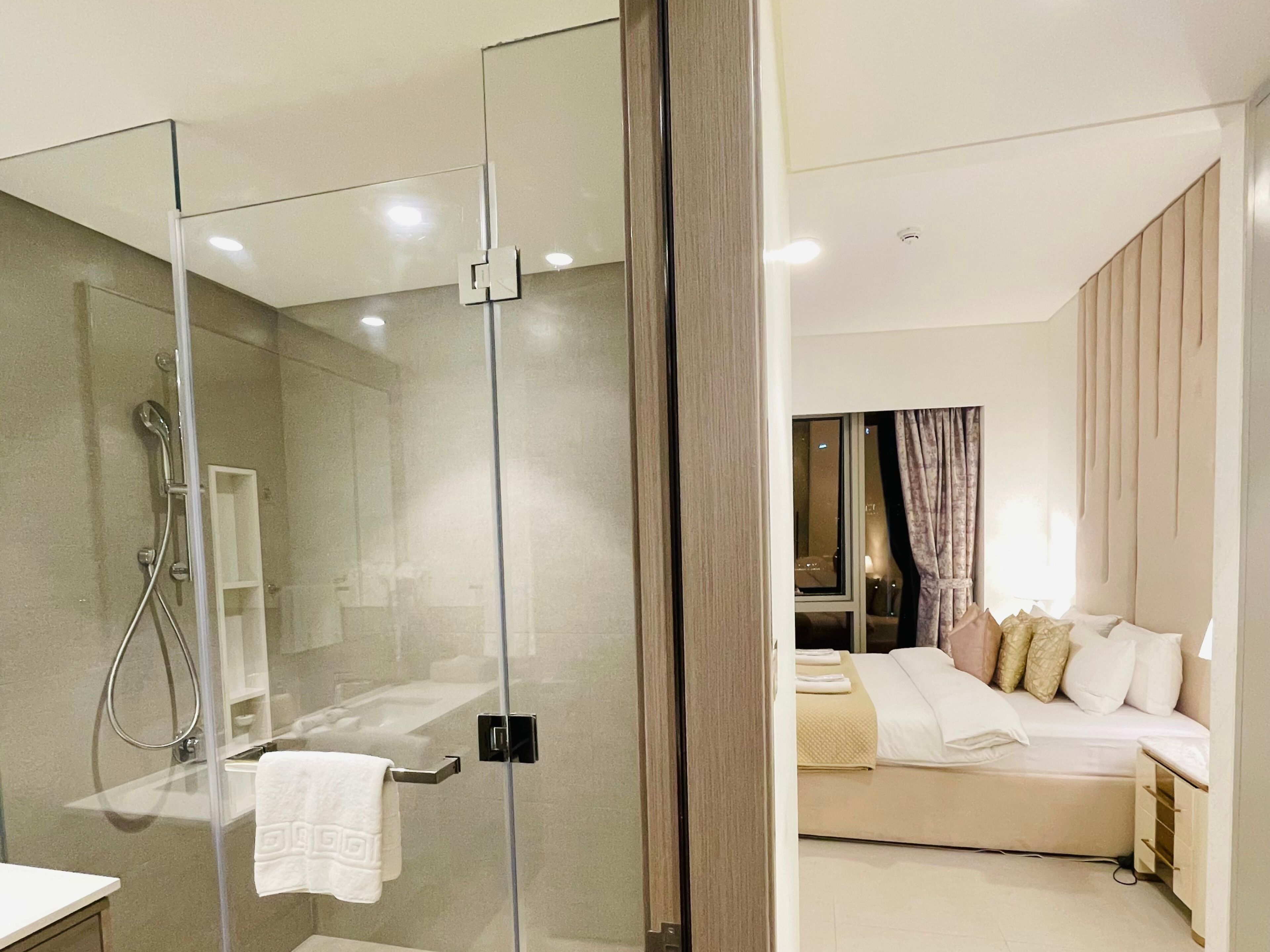 Une chambre d’hôtel moderne dotée d’une douche en verre, d’un lit avec plusieurs oreillers et d’une table de chevet.