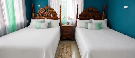 Un dormitorio con dos camas, cabeceros de madera, una mesita de noche, un florero con flores y una alfombra estampada.