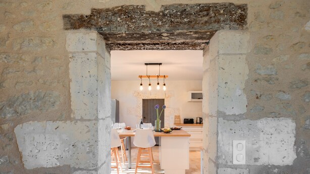 Une cuisine rustique dotée d’un îlot central, d’un coin repas avec des chaises et d’un luminaire suspendu moderne.