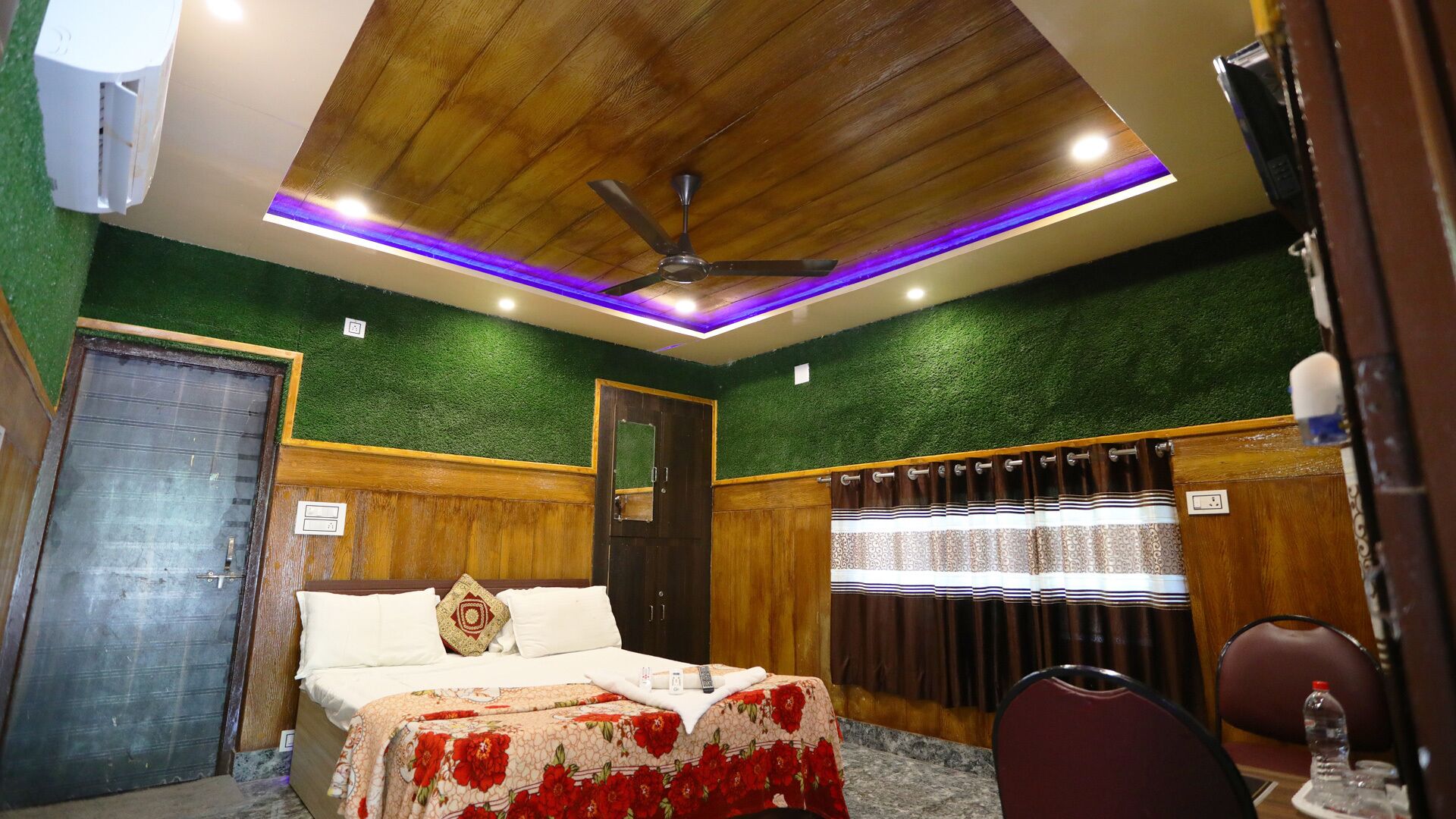 A hotel room with a wooden ceiling, green wall, and a bed with a floral bedspread.