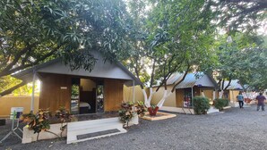 A row of small, single-story buildings with a gravel courtyard, each with a covered entrance and a small porch area. - Shree Murlidhar Farm and resort (Mendarda)