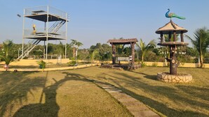 A park with a playground structure, a gazebo, and a decorative bird sculpture. - Shree Murlidhar Farm and resort (Mendarda)