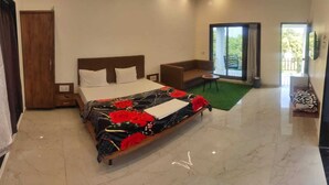 A modern hotel room with a large bed, a sofa, a small table, and a view of the outdoors. - Shree Murlidhar Farm and resort (Mendarda)