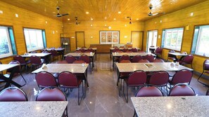A conference room with tables and chairs, wooden walls, and ceiling fans. - Shree Murlidhar Farm and resort (Mendarda)