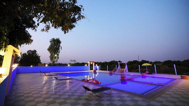 A pool area with lounge chairs, a covered seating area, and a checkered floor. - Shree Murlidhar Farm and resort (Mendarda)