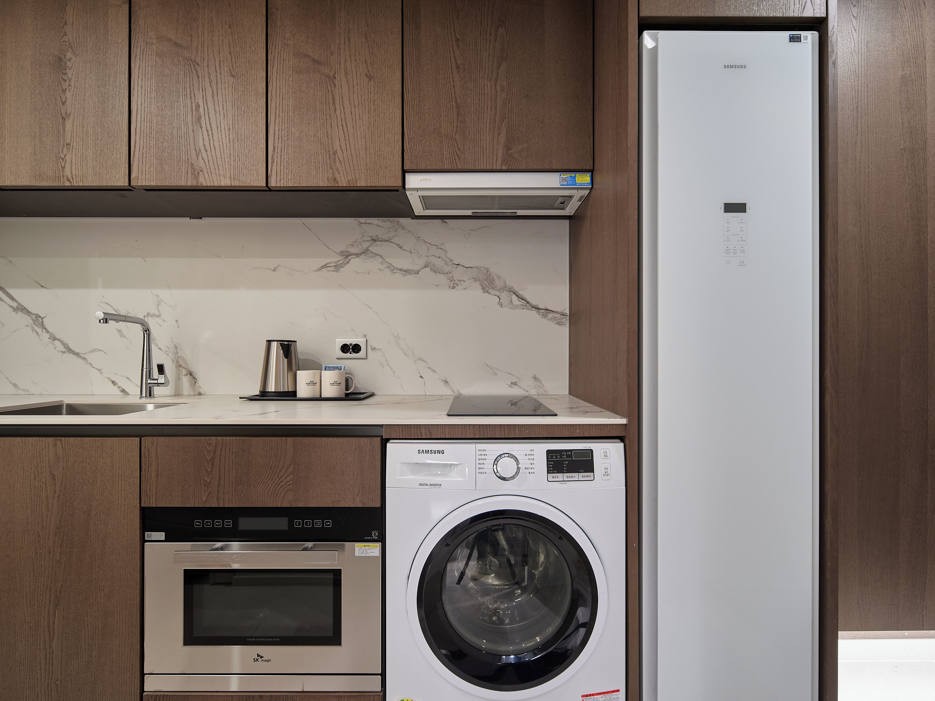 A kitchen with a built-in dishwasher, a stainless steel oven, a washing machine, and a Samsung refrigerator.