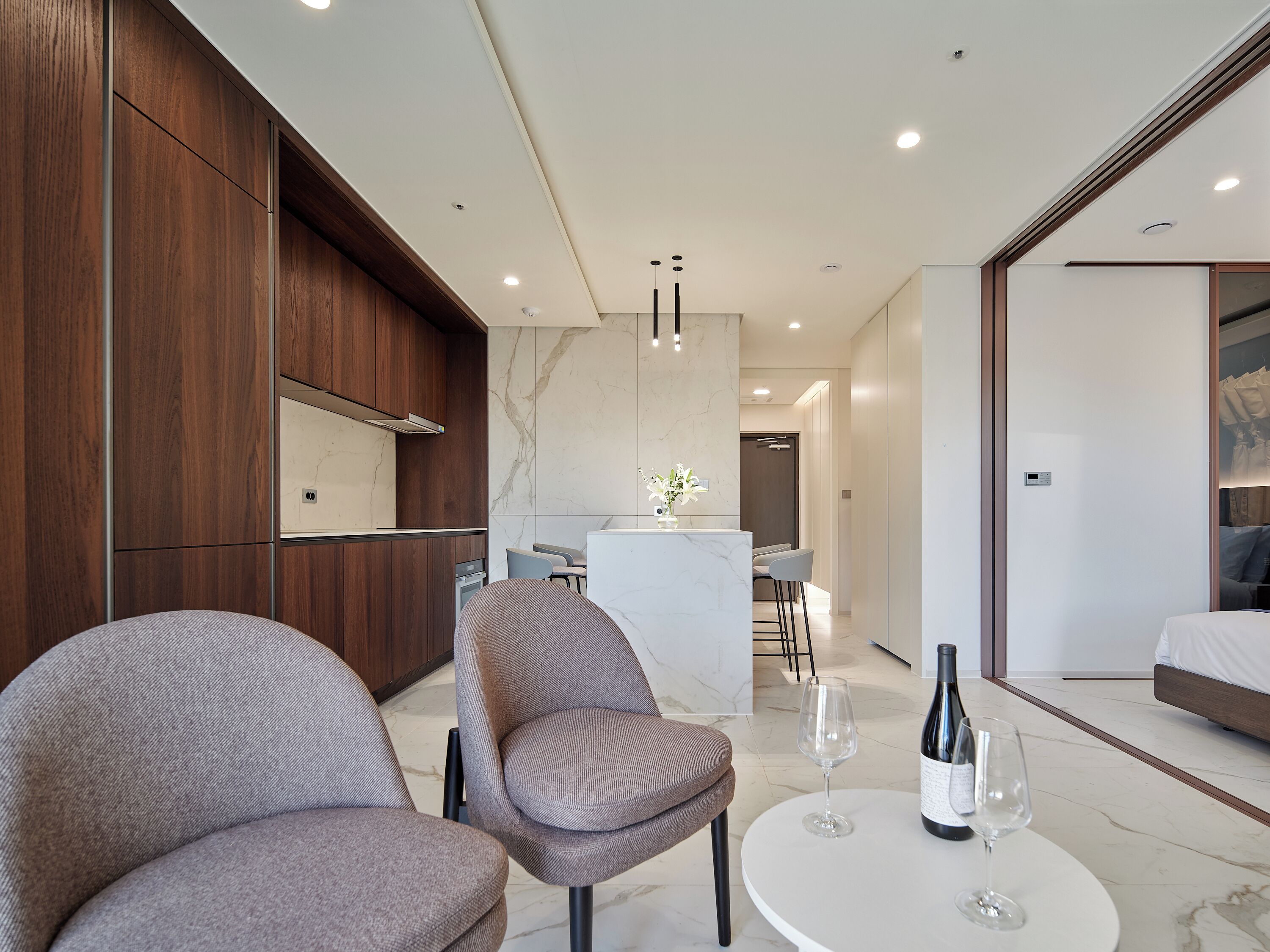 Una habitación de hotel moderna con comedor, sofá y una mesa con copas y botellas de vino.