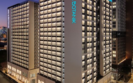 A modern hotel building with multiple floors, large windows, and a prominent sign reading "HOTEL THE BOTANK".