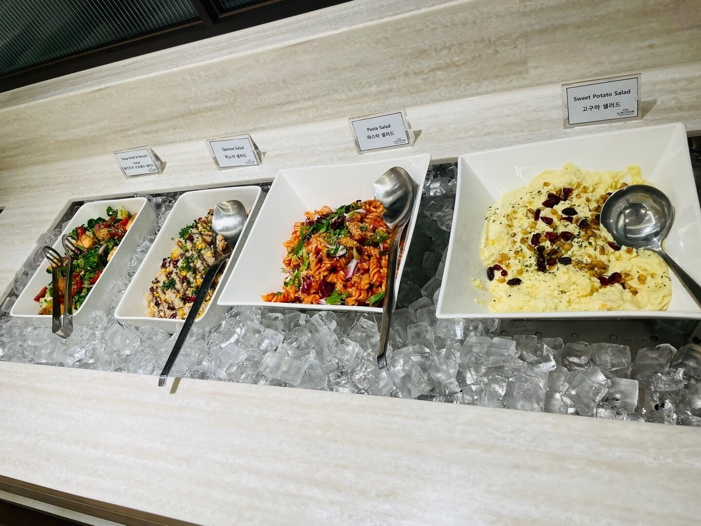 A buffet with three dishes: Quinoa Salad, Pasta Salad, and Sweet Potato Salad.