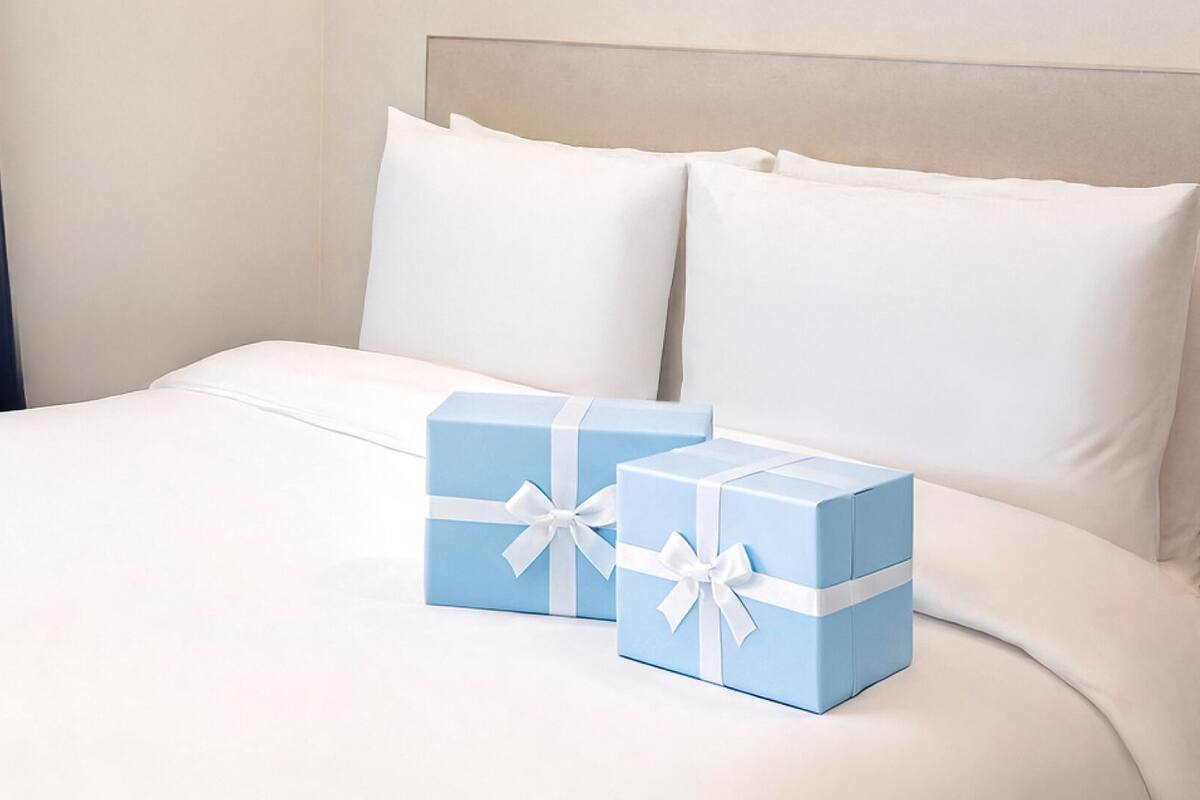 A hotel room with a bed, white bedding, and two blue gift boxes with white ribbons.
