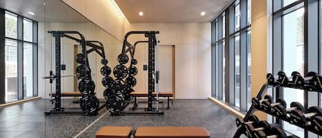 A gym with weightlifting equipment, benches, and a mirrored wall.