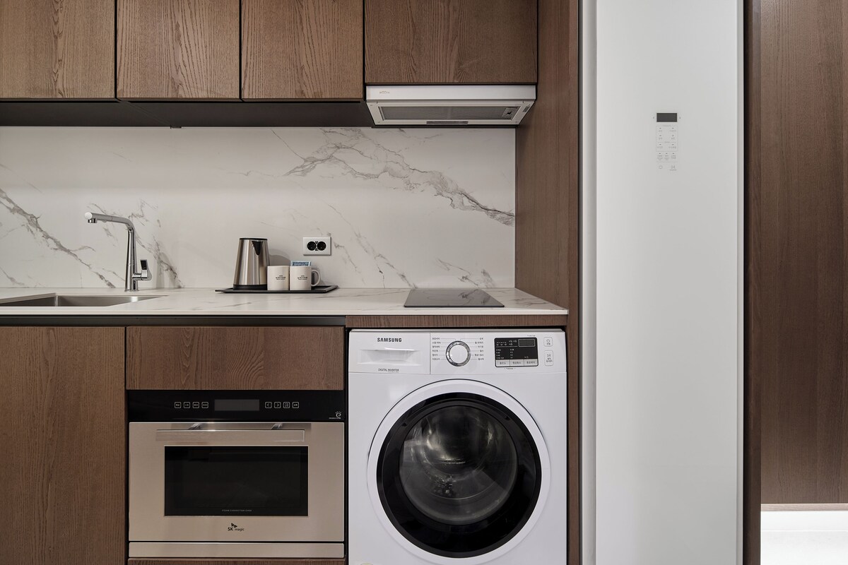 A kitchen with wooden cabinets, a stainless steel sink, a built-in oven, a washing machine, and a Samsung refrigerator.