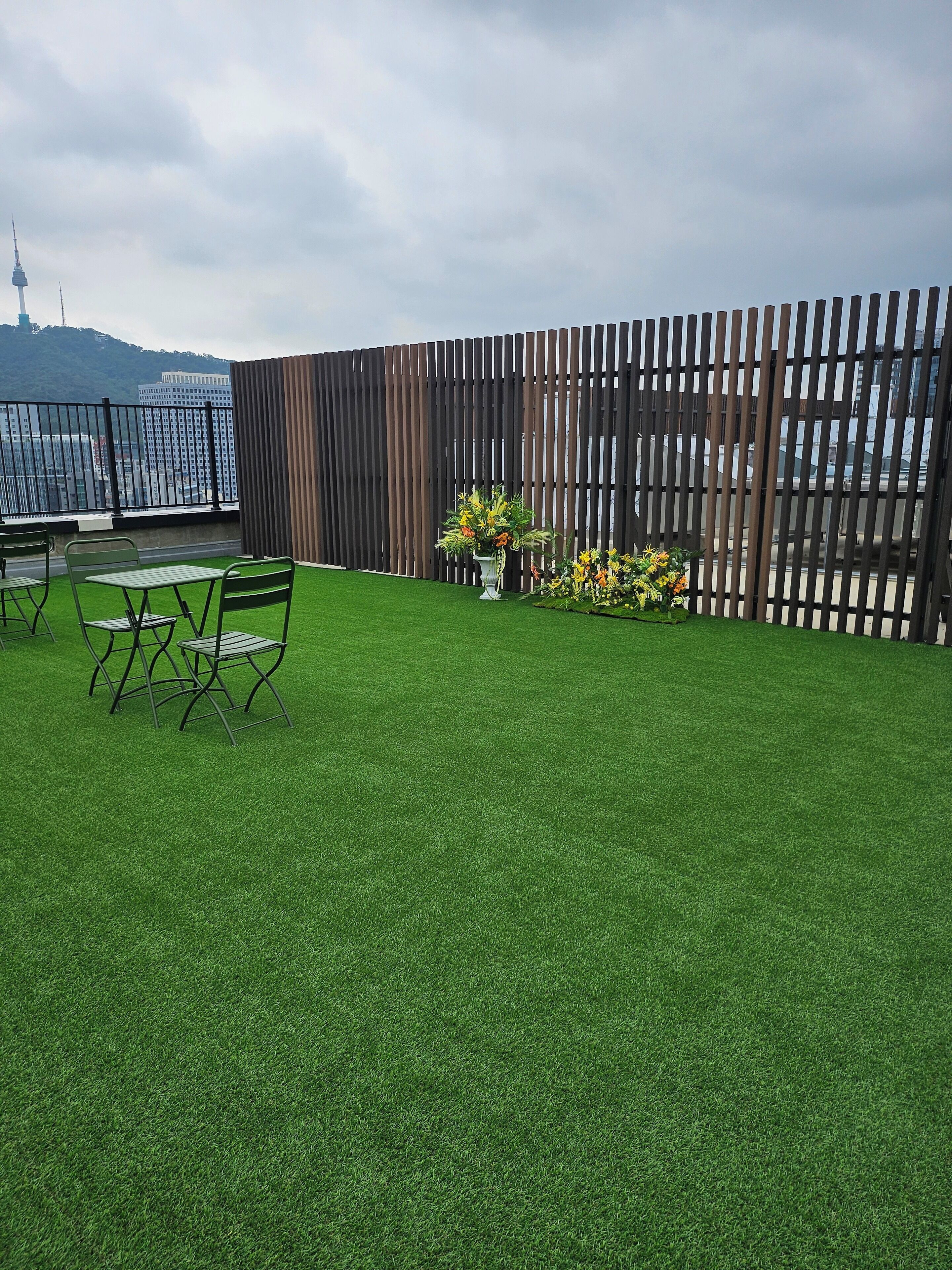 A rooftop garden with artificial grass, a wooden fence, and a small table with chairs.