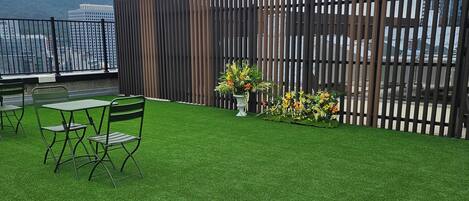 Un jardín en la azotea con césped artificial, una cerca de madera y una pequeña mesa con sillas.