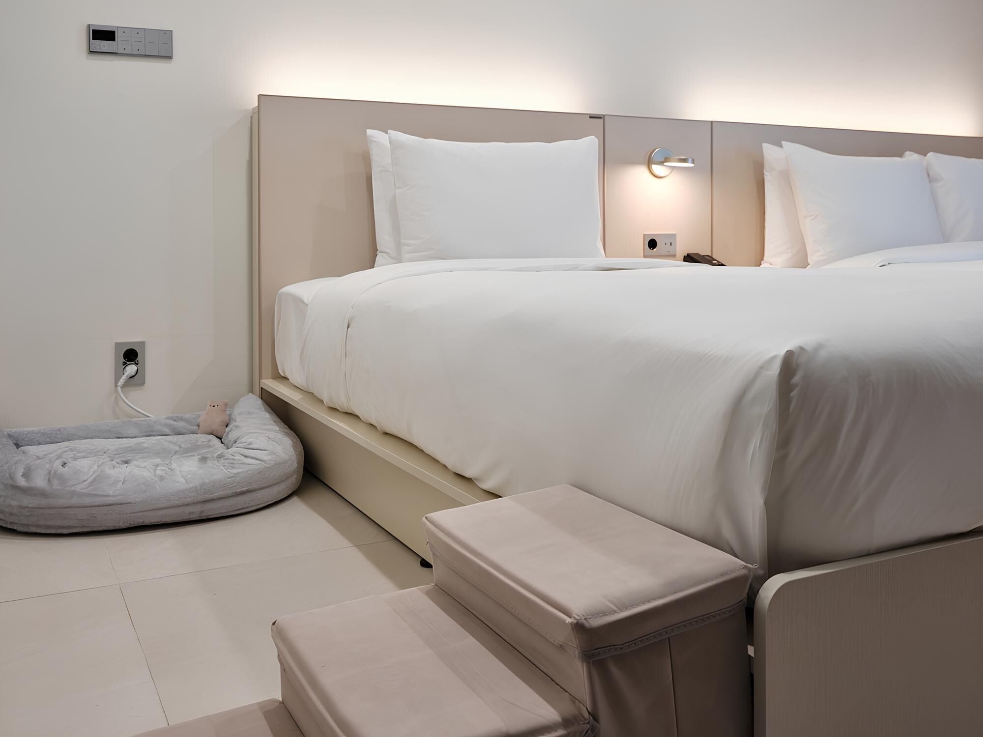 A modern bedroom with a bed, bedside tables, a bedside lamp, a charging station, and a pet bed.