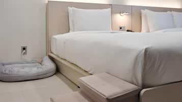A modern bedroom with a bed, bedside tables, a bedside lamp, a charging station, and a pet bed.