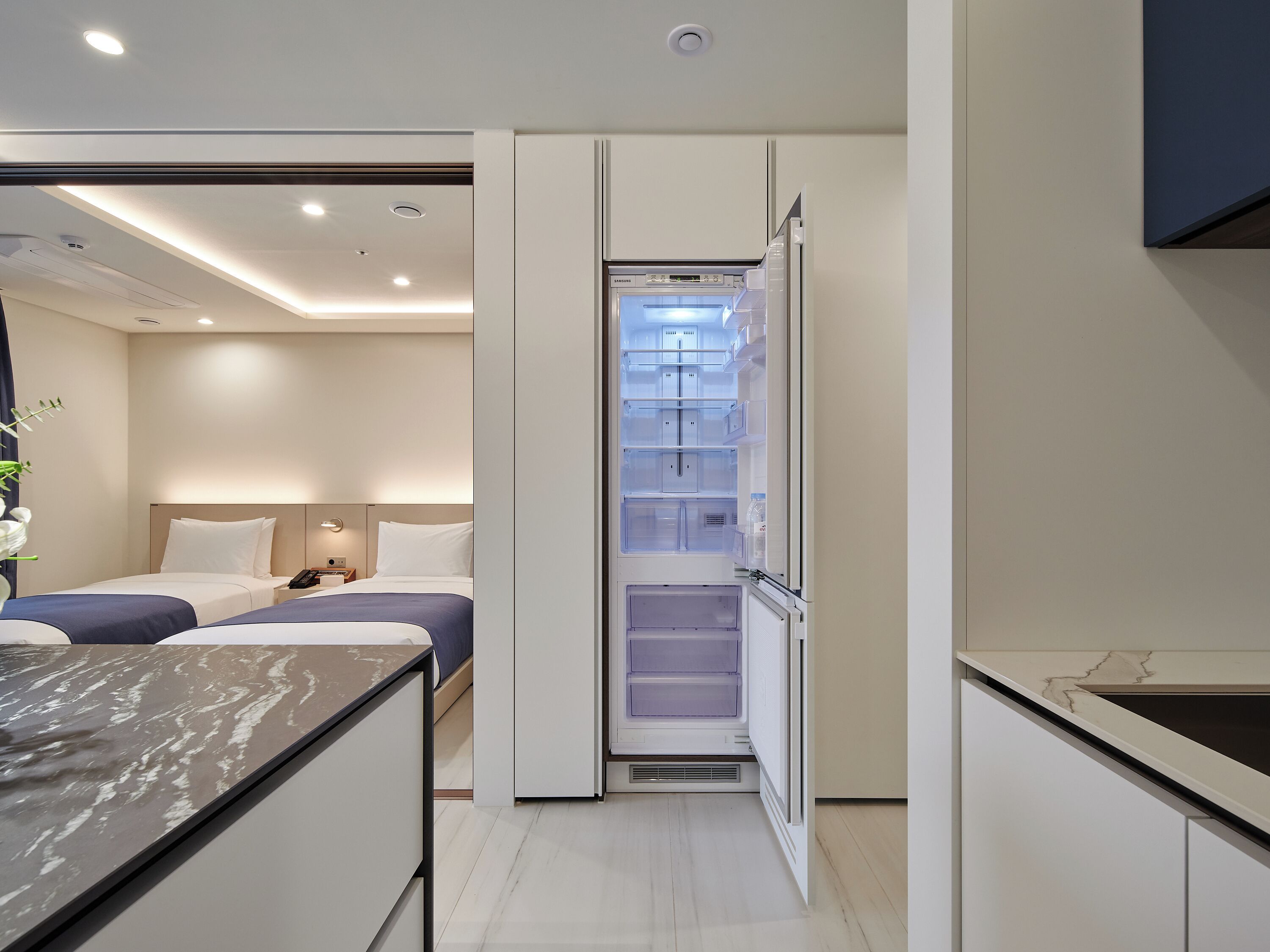 Una habitación de hotel moderna con dos camas, un escritorio integrado y un refrigerador pequeño.