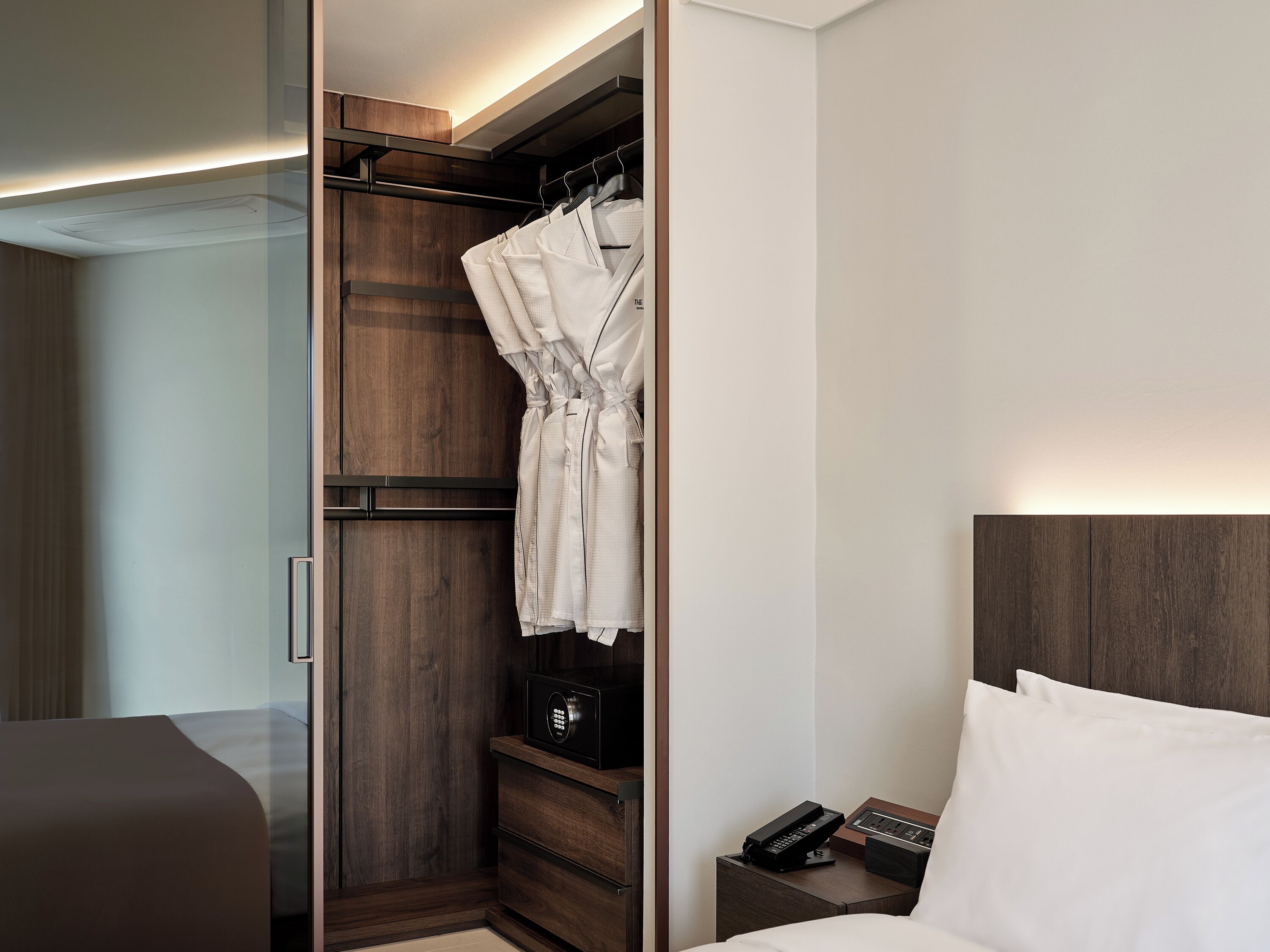 Une chambre d’hôtel dotée d’un dressing, d’une table de chevet avec un téléphone et une radio, et d’un lit avec du linge de lit blanc.