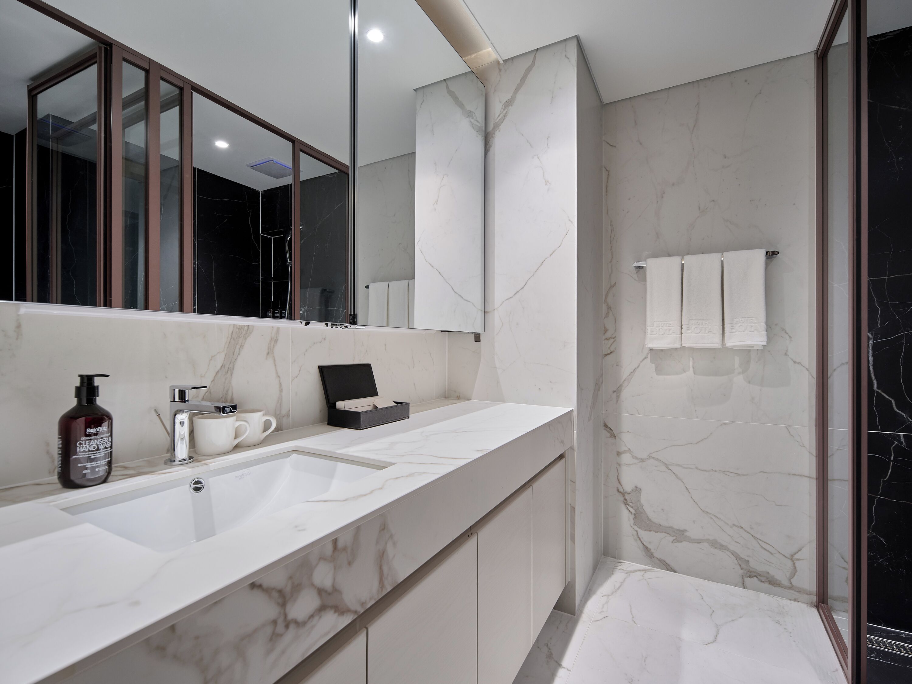Un baño moderno con un espejo grande, un lavabo de mármol blanco y una cabina de ducha de vidrio.
