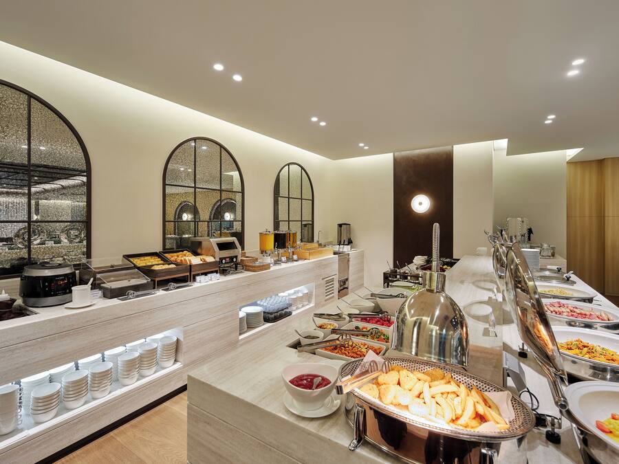 A buffet setup with various food stations, including a coffee machine, a fruit bowl, and multiple serving dishes.