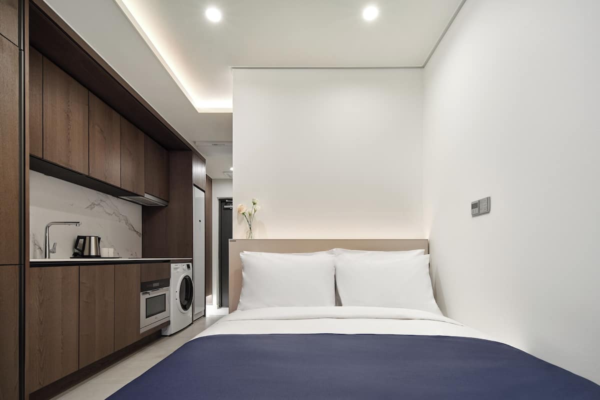 A modern hotel room with a bed, a washing machine, and a small kitchenette.