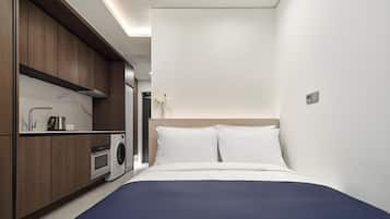 A modern hotel room with a bed, a washing machine, and a small kitchenette.