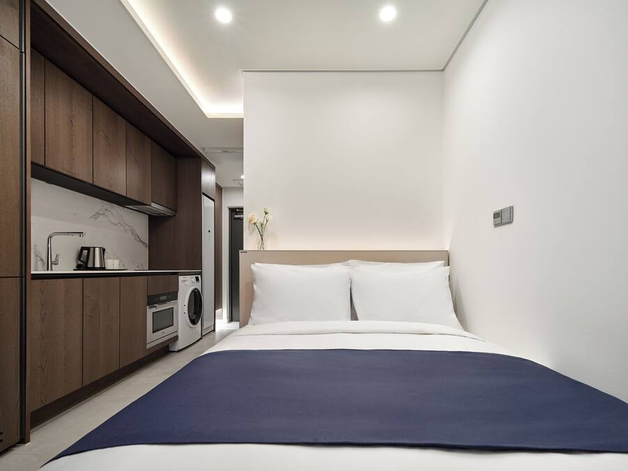 A modern hotel room with a bed, a washing machine, and a small kitchenette.
