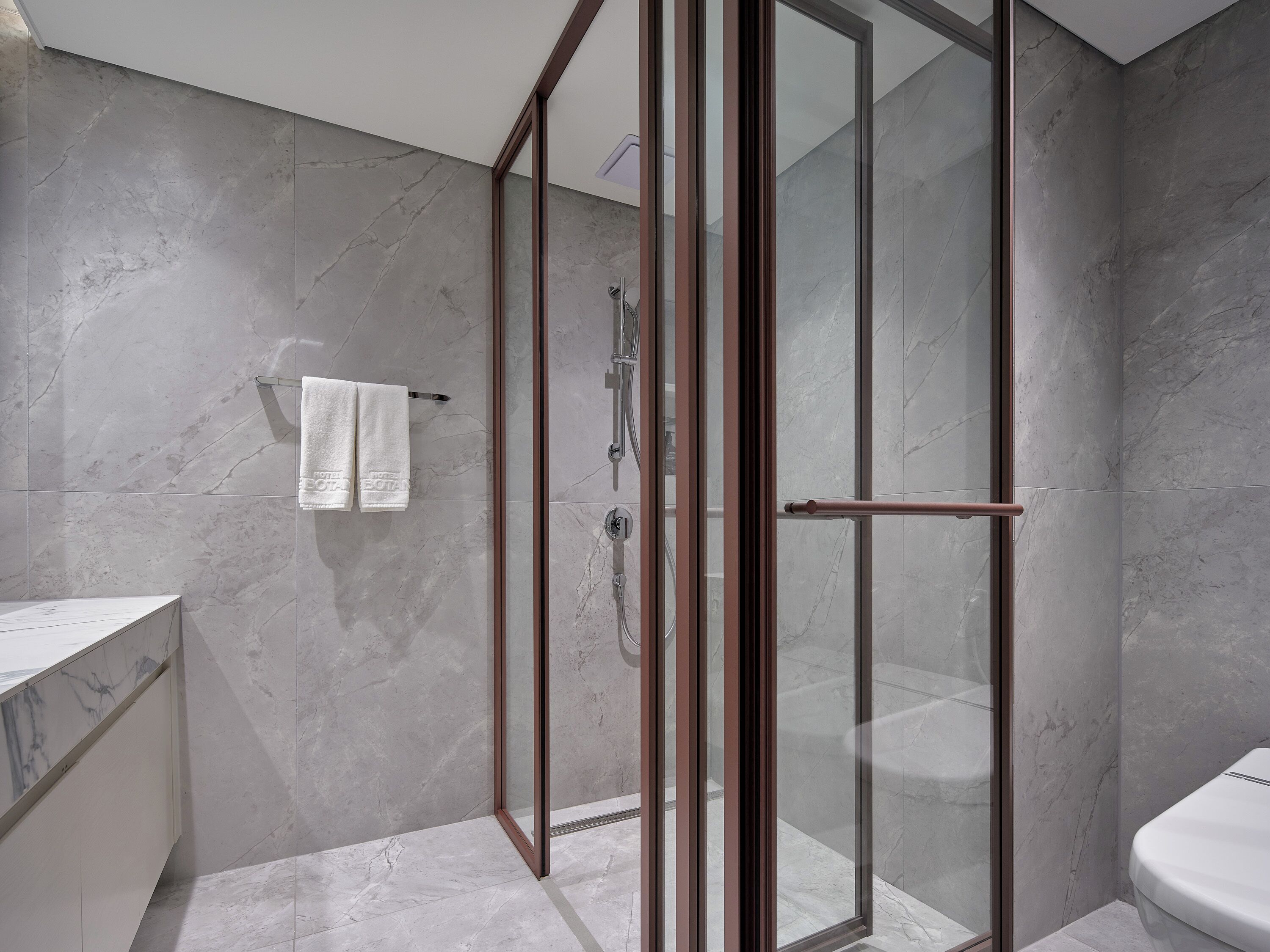 A modern bathroom with a glass shower enclosure, marble flooring, and a white toilet.