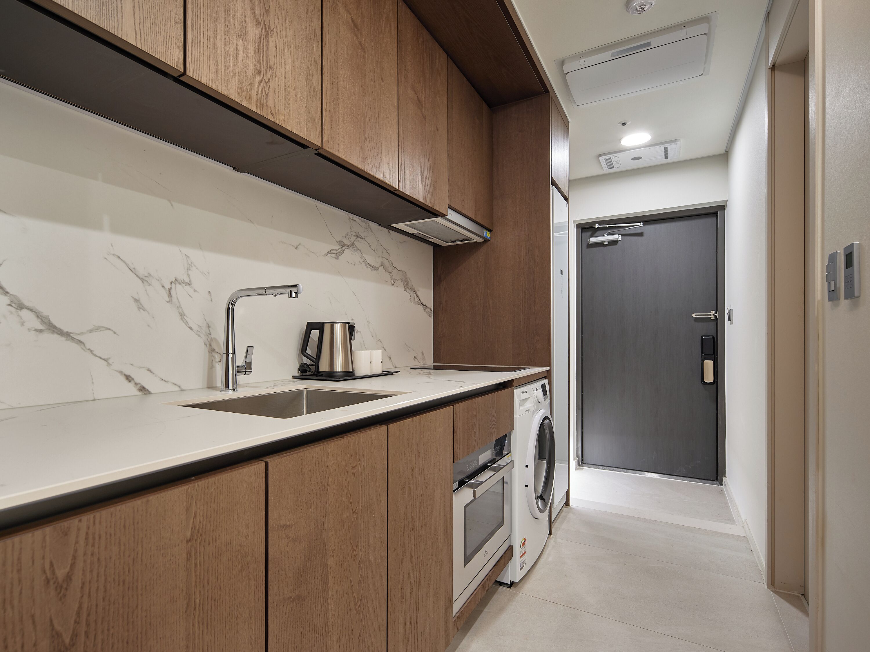 A modern kitchen with a marble backsplash, wooden cabinets, a built-in oven, and a washing machine.