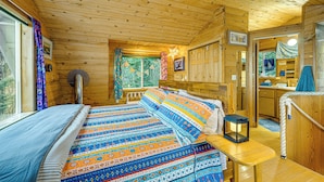 Una cabaña con interior de madera, una cama con ropa de cama estampada, una mesita con un farolillo, y un baño visible a través de una puerta abierta.