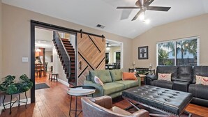A spacious living room with a wooden staircase, a ceiling fan, and a large window.