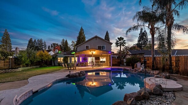 A residential backyard with a swimming pool, patio furniture, and a house with a covered outdoor area.