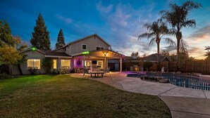 A house with a covered patio, a swimming pool, and a well-maintained lawn.