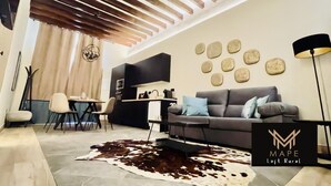 Een moderne woonkamer met een grijze bank, een vachttapijt en een plafond met houten balken.
