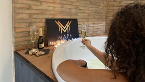 Iemand ontspant in een jacuzzi, met een bord dat 'MAPE APRENDIMIENTO' vermeldt en twee champagneflessen op het aanrecht.