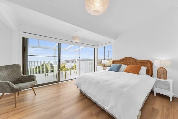 A bedroom with a large bed, a chair, a nightstand, and a view of the outdoors.