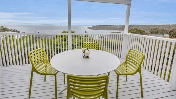 A covered outdoor area with a round table and four chairs, overlooking a body of water and hills. - Pambula Little Beach House (Pambula Beach)