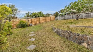 A backyard with a stone wall, a wooden fence, and a paved path. - Pambula Little Beach House (Pambula Beach)