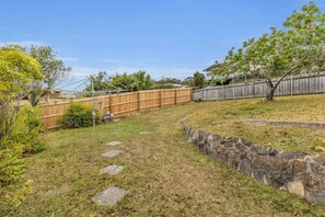 Un jardin avec un mur en pierre, une clôture en bois et un chemin dallé.
