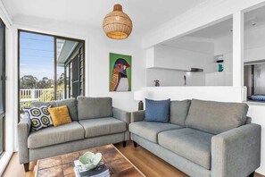 A modern living room with a grey sectional sofa, a coffee table, and a large window with a view of greenery.