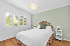 Une chambre à coucher comprenant un lit, une fenêtre avec des stores, une table de chevet avec une lampe et un luminaire fixé au mur.